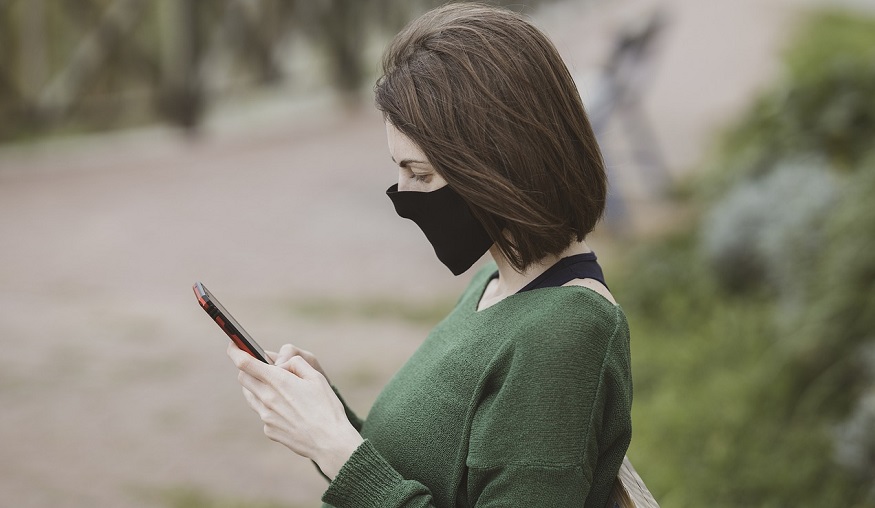 COBRA Insurance - Woman Looking at Phone sitting on bench wearing mask